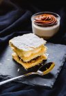 Nahaufnahme von Blätterteig-Dessert mit Sahne auf Schiefer und Dessert in Tasse auf schwarzem Stoff — Stockfoto
