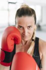 Жінка в боксерських рукавичках стоїть в бойовому положенні і дивиться на камеру під час тренувань — стокове фото