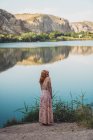 Woman in long summer dress standing on lake shore — Stock Photo