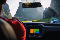 Close-up of man driving car on narrow road between high stunning mountains and grassy fields on sunny day, Guangxi, China — Stock Photo