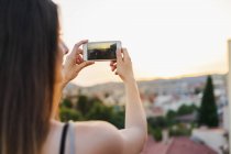 Femme prenant une photo de la ville au coucher du soleil — Photo de stock