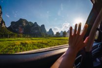 Human hand touching window of car driving through rice paddies and mountains on sunny day, Guangxi, China — Stock Photo