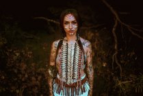 Attraktive junge Frau mit traditionellen indischen Bildern im Gesicht, die in die Kamera blickt und im Wald steht — Stockfoto