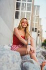 Young woman in red shorts and tank top sitting on stones in city — Stock Photo