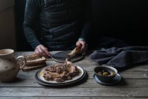 Мужские руки, намазывающие чечевицу на хлеб на деревенском деревянном столе — стоковое фото