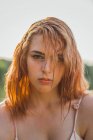 Nahaufnahme einer ernsten jungen Frau mit nassen Haaren und Sommersprossen, die im Sonnenlicht in die Kamera blickt — Stockfoto