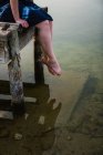 Крупным планом ног женщины, сидящей на пирсе у озера — стоковое фото