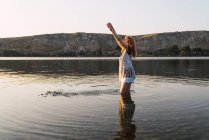 Donna in piedi in acque limpide del lago con le braccia alzate — Foto stock