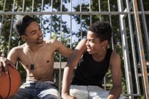 Afro jovens irmãos sentados com basquete na quadra ao ar livre e abraçando — Fotografia de Stock