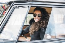 Retrato de jovem mulher de casaco preto e óculos de sol sentado dentro do carro — Fotografia de Stock