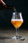 Menschliche Hand gießt Bier aus Flasche in Glas auf grauem Hintergrund — Stockfoto