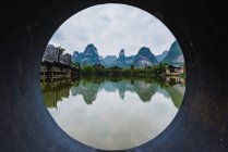 View through round pipe of water surface of Quy Son river, wooden flooring and buildings of harbor, Guangxi, China — Stock Photo