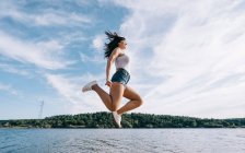 Cheerful woman jumps by the lake. — Stock Photo