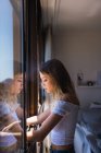 Nachdenkliche junge Frau schaut zu Hause aus dem Fenster — Stockfoto