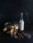 Disposizione rustica di riso, latte, spezie e limoni su tavolo di legno nero con utensile — Foto stock