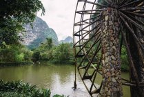 Деревянное водяное колесо старой каменной водяной мельницы в деревьях на берегу реки Quy Son с великолепными горами на заднем плане, Гуанси, Китай — стоковое фото
