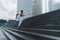 Молодой человек в спортивной одежде бегает по лестнице со стеклянными современными зданиями на заднем плане — стоковое фото
