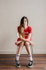 Hübsche junge Frau in rotem Outfit sitzt auf Stuhl und schaut in die Kamera — Stockfoto