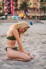 Весела жінка в бікіні сидить на піску і дивиться на камеру — стокове фото