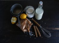 Disposizione rustica di riso, latte, spezie e limoni su tavolo di legno nero con utensile — Foto stock