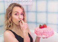 Чувственная женщина в черном нижнем белье сидит в ванной и пробует сладкий крем из вкусного торта — стоковое фото
