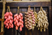 Chinese sweet potatoes with peanuts and garlic hanging in bunches on wooden wall — Stock Photo