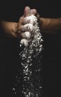 Mani umane scuotendo farina e pezzi di pasta su sfondo nero — Foto stock