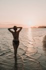 Donna in costume da bagno in piedi in mare in luci del tramonto — Foto stock