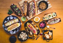 Vari hot dog serviti con diversi condimenti e spuntini sul tavolo di legno — Foto stock