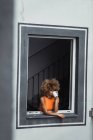 Curly ethnic woman holding cup and looking out of window — Stock Photo