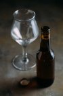 Bottiglia di birra e bicchiere vuoto su sfondo grigio — Foto stock