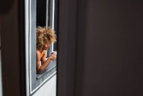 Кучерява етнічна жінка тримає чашку і дивиться з вікна — стокове фото