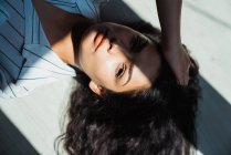 Giovane donna bruna pensosa con i capelli lunghi sdraiata sul pavimento in ombra e luce solare — Foto stock