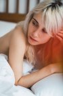 Shirtless blonde woman lying on comfortable bed in cozy bedroom — Stock Photo