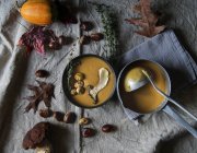 Soupe à la crème de citrouille dans un bol avec casserole et louche sur tissu rustique — Photo de stock