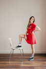 Усміхнена дівчина в червоному вбранні позує з однією ногою на стільці — стокове фото