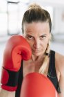 Frau in Boxhandschuhen steht in Kampfposition und blickt beim Training in die Kamera — Stockfoto