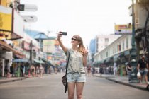 Веселий жінка прийняття selfie і жестикулюючи два пальці на вулиці в Таїланді — стокове фото