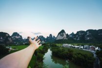Mão humana mostrando no cénico rio Quy Son com cidade em montanhas ao entardecer, Guangxi, China — Fotografia de Stock