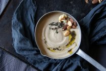Creamy cauliflower soup with almonds in saucepan on tray with cloth — Stock Photo