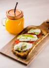 Golden bread toast with tomatoes and white cheese topped on wooden board with glass of juice — Stock Photo