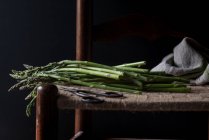 Крупним планом пучок свіжої зеленої спаржі на стільці на чорному фоні — стокове фото