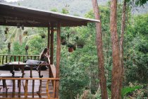 Жінка сидить на терасі в тропічній природі і дивиться на пальми — стокове фото