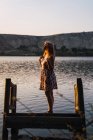 Mulher sonhadora em vestido de verão em pé no cais afundado no lago — Fotografia de Stock