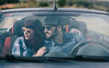 Brunette woman in casual clothes and bearded man in shirt sitting in dark car and looking away — Stock Photo