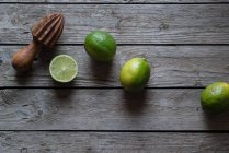 Lime fresco intero e dimezzato con spremiagrumi in legno su legno grigio — Foto stock
