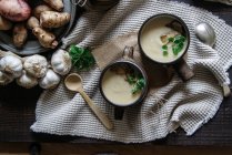 Cuencos de sabrosa sopa de alcachofa de Jerusalén con ingredientes en la mesa de madera rústica - foto de stock