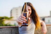 Щаслива жінка показує пляшку коричневого пива на даху — стокове фото