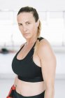 Selbstbewusste Frau in Sportbekleidung steht auf verschwommenem Hintergrund des Fitnessstudios und blickt in die Kamera — Stockfoto