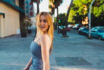 Sorrindo jovem mulher em roupa elegante olhando para a câmera enquanto em pé na rua — Fotografia de Stock
